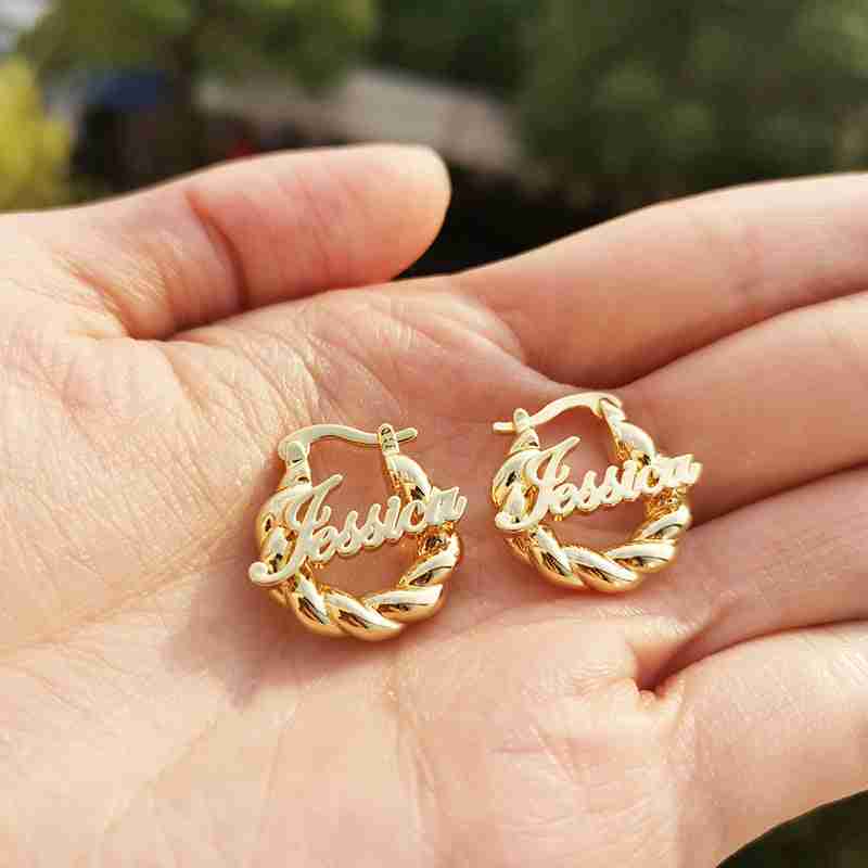 Close-up of gold personalized name earrings with 'Jessica' script and twisted hoop design, stylish jewelry piece