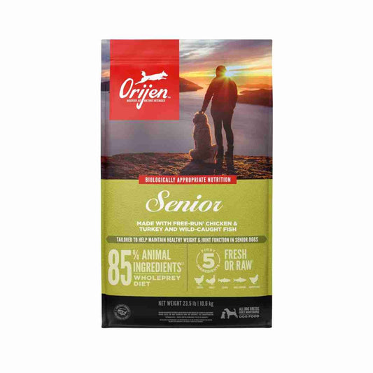 Red and green bag of ORIJEN Senior Dry Dog Food with a sunset background, featuring a person walking a dog on a beach, 23.5lb