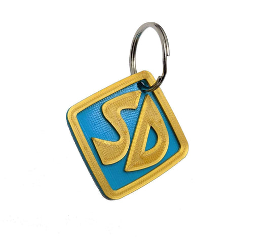 Silver metal ring attached to a yellow and blue dog tag featuring a Superman logo, designed for Halloween dog costume accessories.