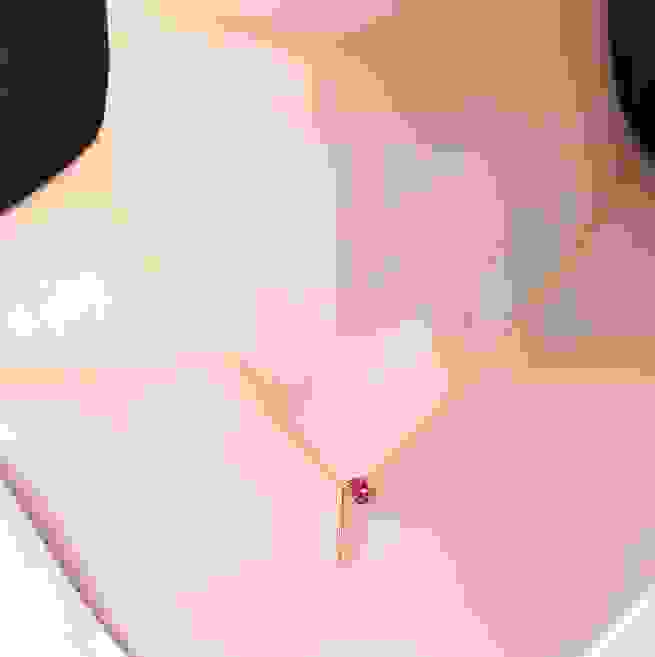 Close-up of a delicate gold necklace with a pink moonstone and red diamond pendant worn on a model with pink top, SKU: 1775241855775109121